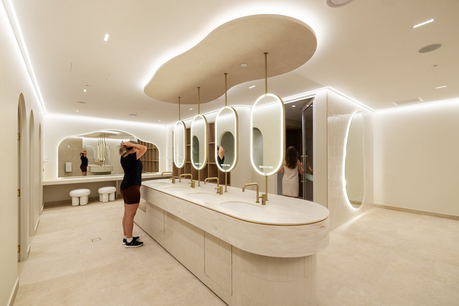 The vanity room with four oval backlit mirrors suspended from brass rods over a stone basin run
